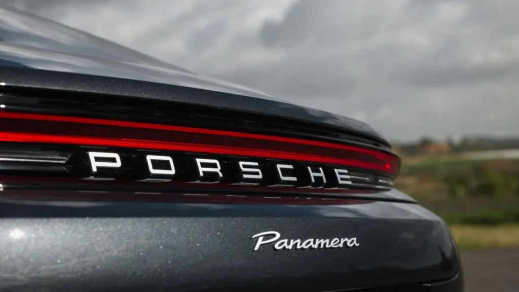 Close-up shot of the rear tailgate and taillight of a dark metallic grey Porsche Panamera showing the silver Porsche lettering and cursive Panamera emblem.