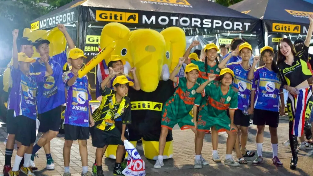 Young football fans celebrating alongside a yellow elephant mascot wearing a Giti Motorsport shirt under a Giti Motorsport canopy tent.