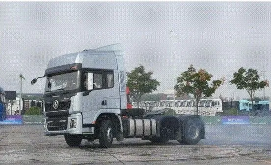 A silver Shacman prime mover executing a sharp turn on a paved test track with tire smoke billowing behind its rear axle.